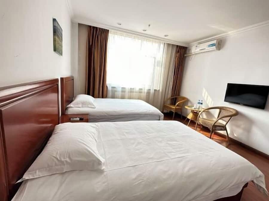 A hotel room with two beds, a television, a chair, and a window with curtains.
