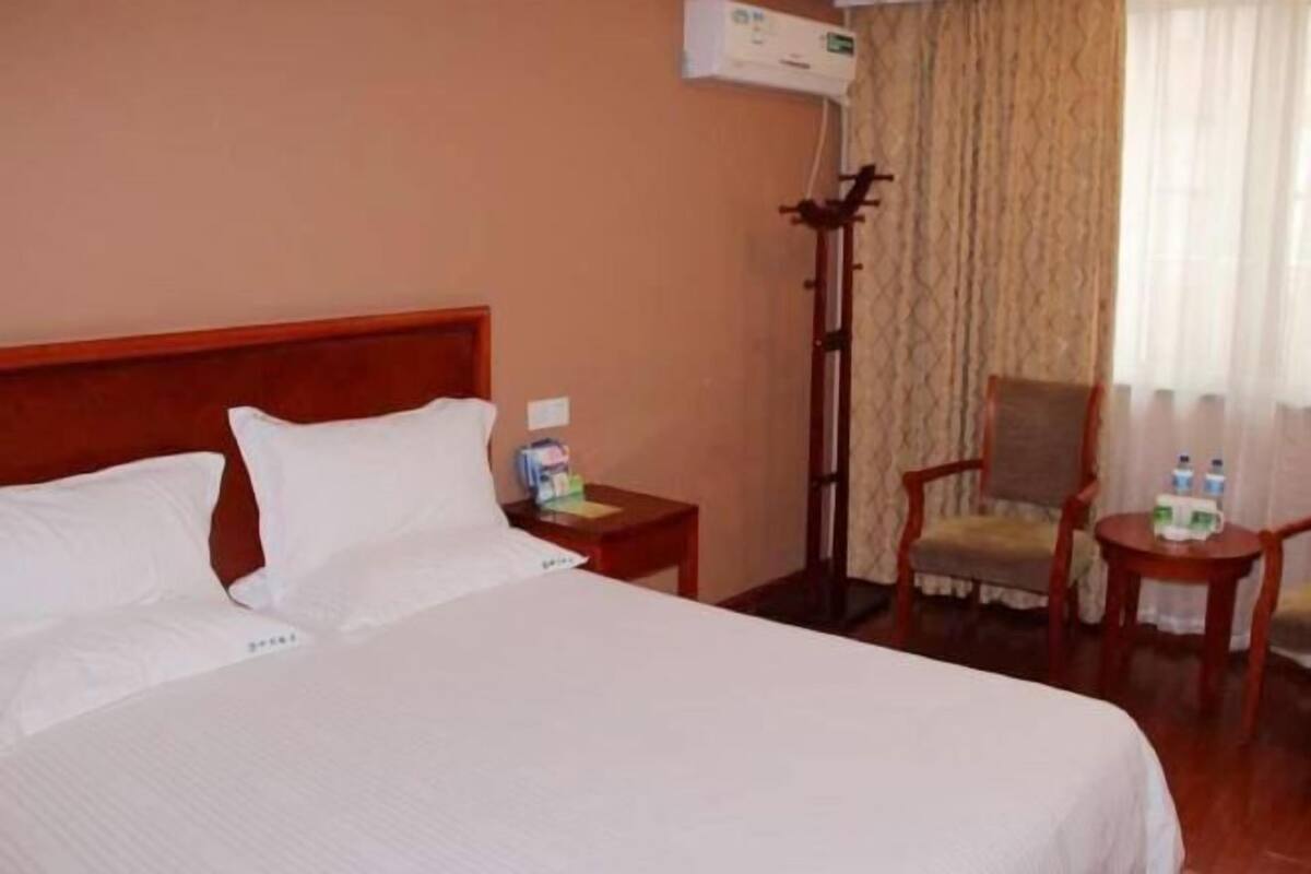 A hotel room with a large bed, a nightstand with a lamp, a chair, and a small table with water bottles.