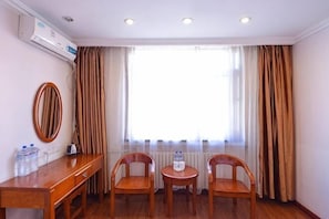A hotel room with a wooden desk, two chairs, a round table, a mirror, and a large window with curtains.
