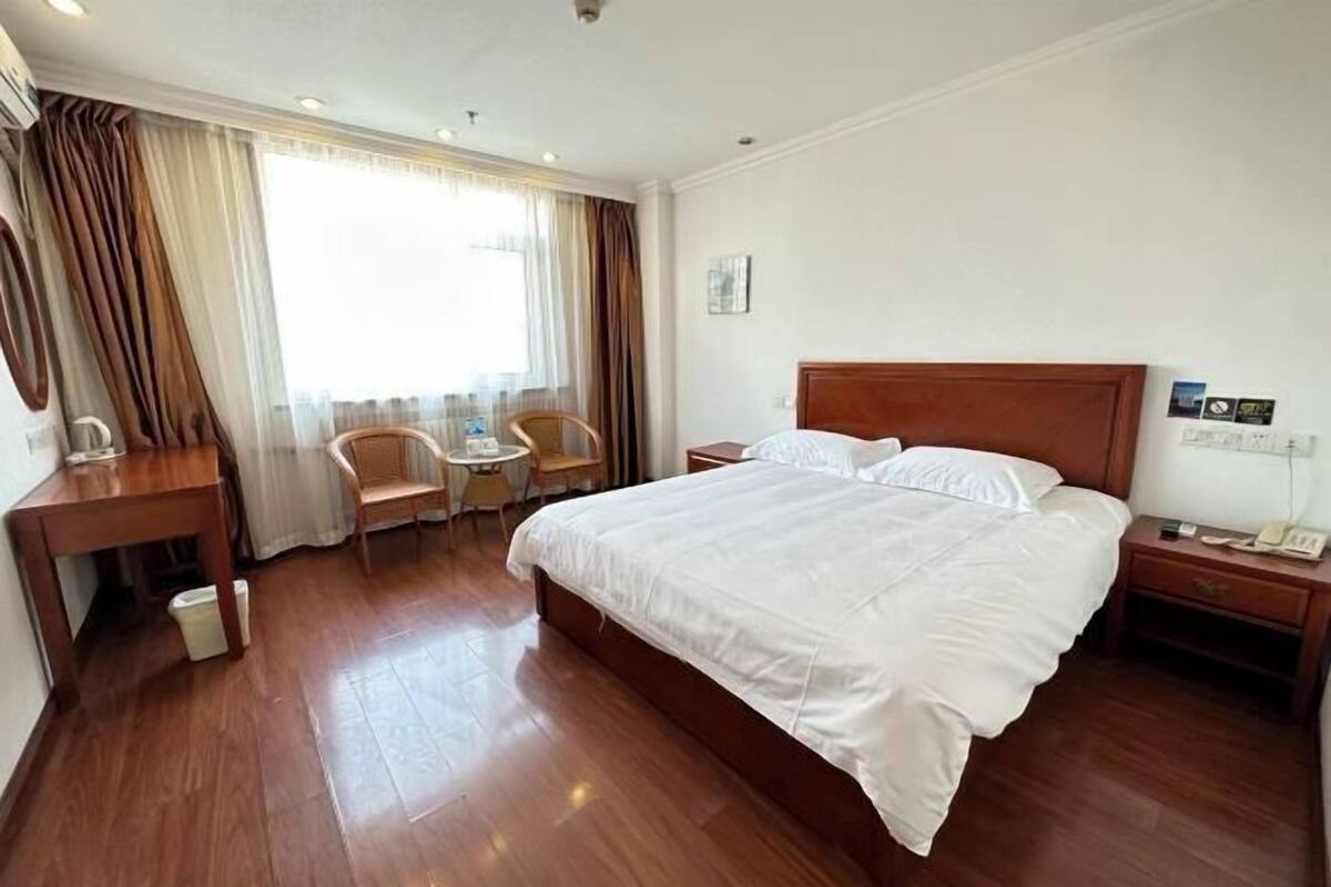 A hotel room with a large bed, a desk, a chair, a small table, and a window with curtains.