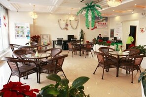 Un hall d’hôtel avec des tables rondes et des chaises en osier, un comptoir d’accueil et un mur sur lequel est affiché un panneau.