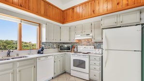 A kitchen with white cabinets, a stove, a microwave, and a refrigerator. - Dolphin Days Hot Tub, Pool & steps to the Beach (Corolla)