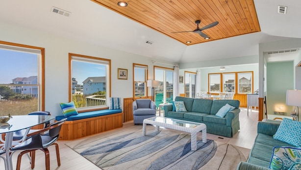 A spacious living area with a high ceiling, large windows, and a view of the outside. - Dolphin Days Hot Tub, Pool & steps to the Beach (Corolla)