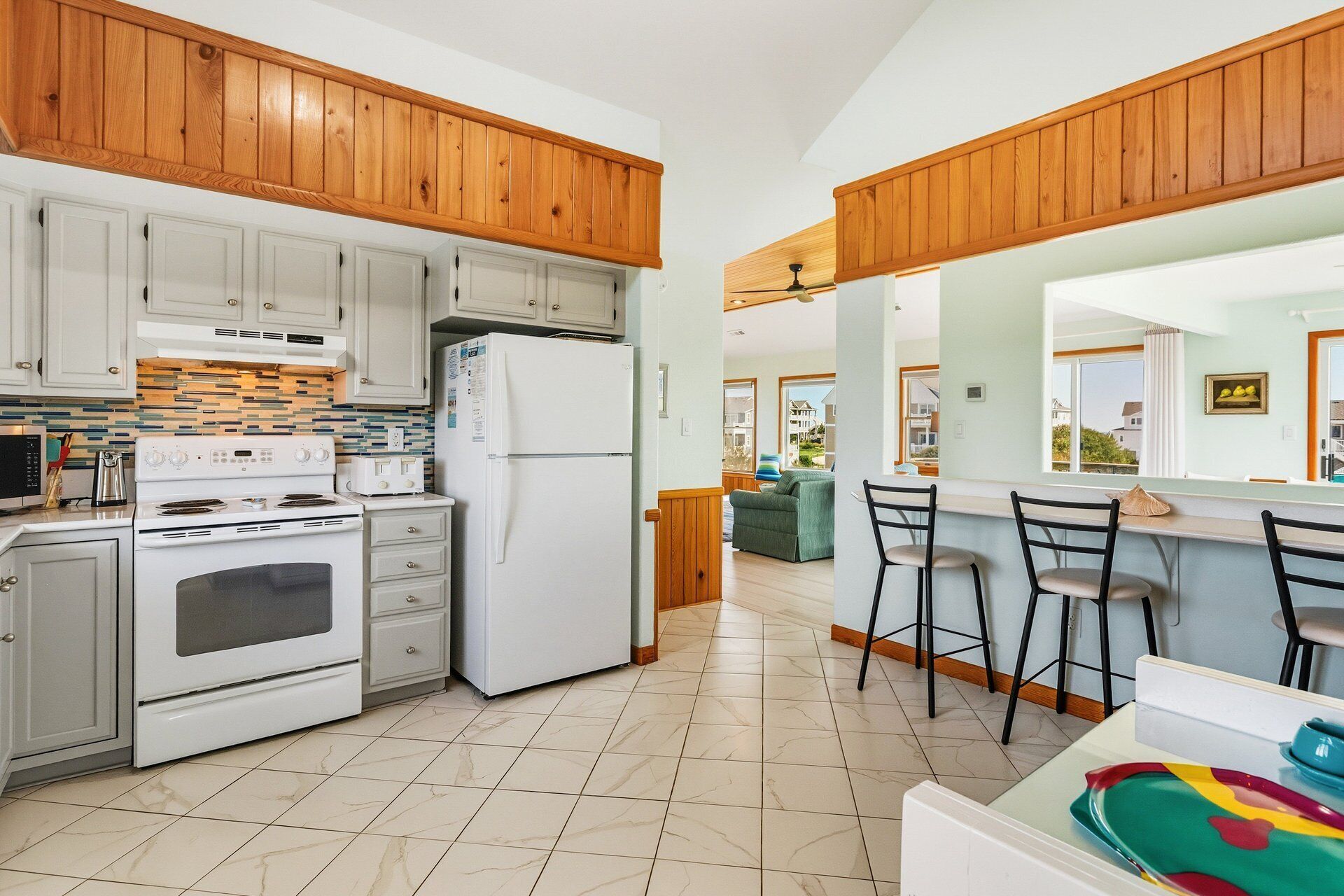 A modern kitchen with white appliances, wooden cabinets, and a dining area with bar stools.