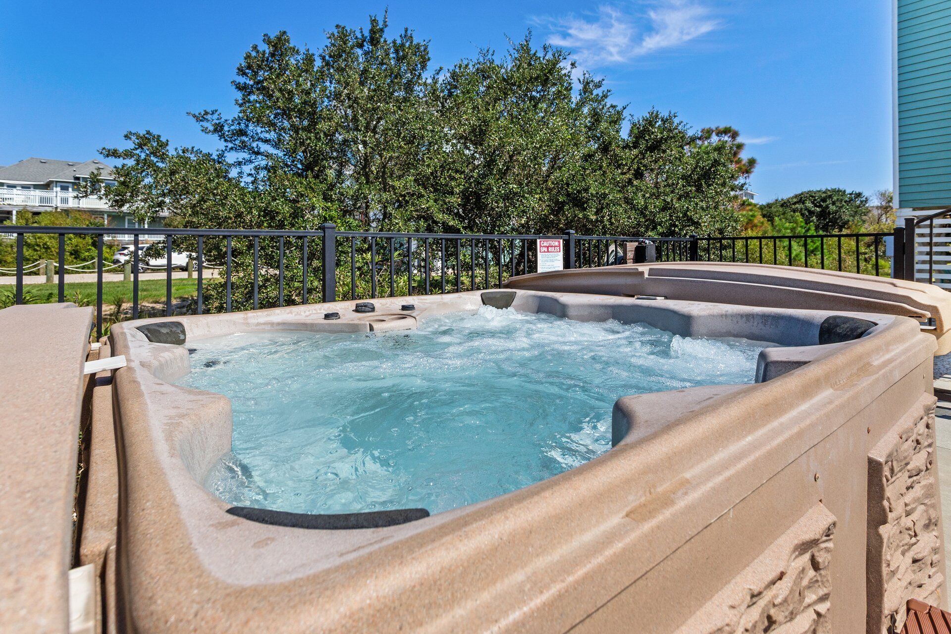 A hot tub with a stone exterior, surrounded by a metal railing, and a caution sign nearby.