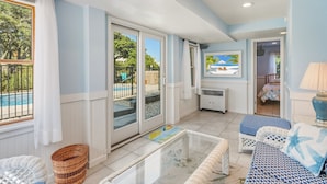 A room with a glass door leading to a pool area, a sofa, a small table, and a lamp. - Dolphin Days Hot Tub, Pool & steps to the Beach (Corolla)