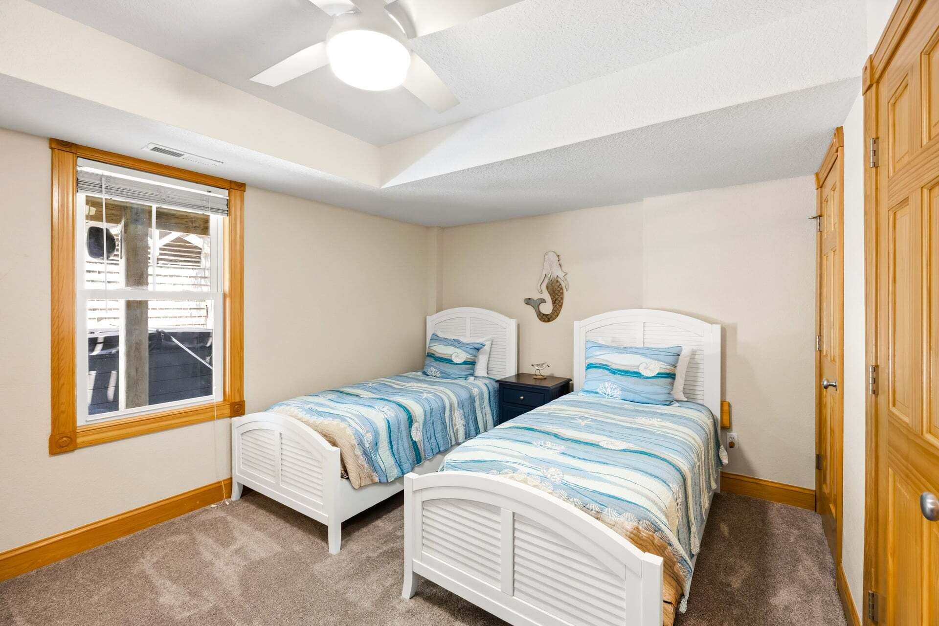 A bedroom with two beds, a window, a ceiling fan, and a wooden door.