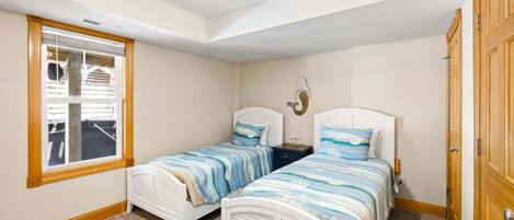 A bedroom with two beds, a window, a ceiling fan, and a wooden door.