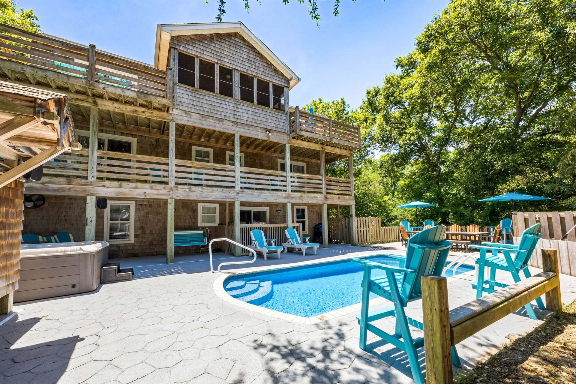 Un edificio de madera de dos pisos con piscina, asientos exteriores y un patio cubierto.