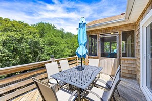 A wooden deck with a table and chairs, a blue umbrella, and a view of a forest. - Big Guppy: Pool, Elevator, Hot Tub, Dog-Friendly (Duck)
