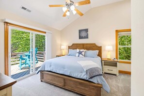 Ein Schlafzimmer mit einem Bett, zwei Nachttischen, einem Deckenventilator, einem Fenster und Blick auf eine Terrasse.