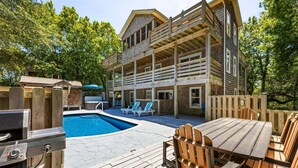 Een houten chalet met zwembad, terras en barbecue.