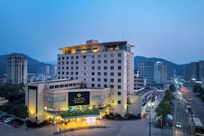 A multi-story hotel with a prominent sign, a parking area, and a cityscape in the background.