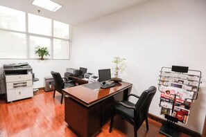 A modern office with a wooden desk, two chairs, a printer, a computer, and a magazine rack. - Zhongwei Sunny Hotel (Jinyun)