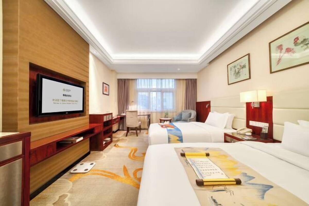 A hotel room with a television, a desk, a chair, a bed, and a window.
