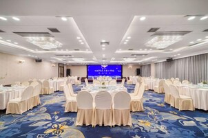 A conference room with round tables, chairs, and a stage with a blue screen.