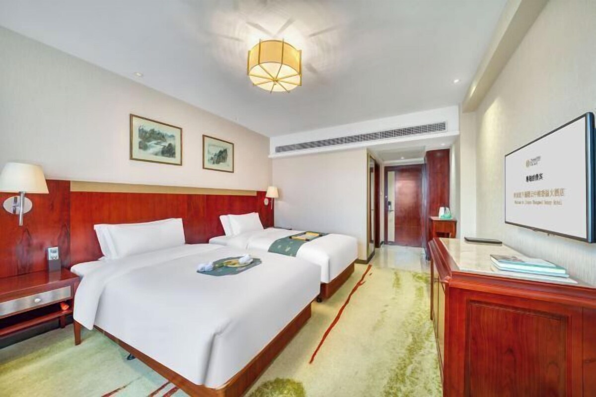 A hotel room with two beds, a wooden headboard, a desk, a chair, a lamp, and a framed picture on the wall.