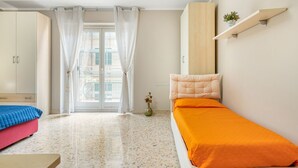 Un dormitorio con cama, armario, estante con planta y ventana con cortinas.