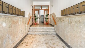 Un pasillo con piso de mármol, taquillas, una escalera y plantas en macetas.