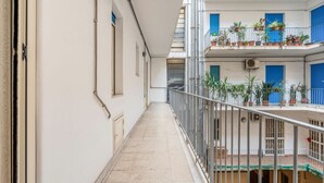 Un pasillo con barandilla de metal, plantas en macetas en los balcones y suelo de baldosas.