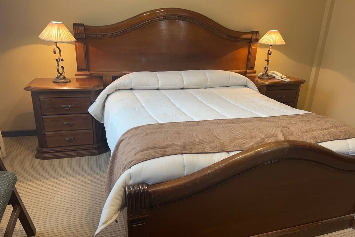 A neatly made bed with a wooden headboard, two bedside tables with lamps, and a wooden nightstand with a lamp.