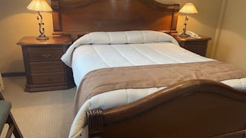 A neatly made bed with a wooden headboard, two bedside tables with lamps, and a wooden nightstand with a lamp.