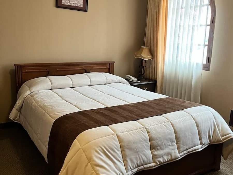 A neatly made bed with a wooden headboard, a bedside lamp, and a framed picture on the wall.