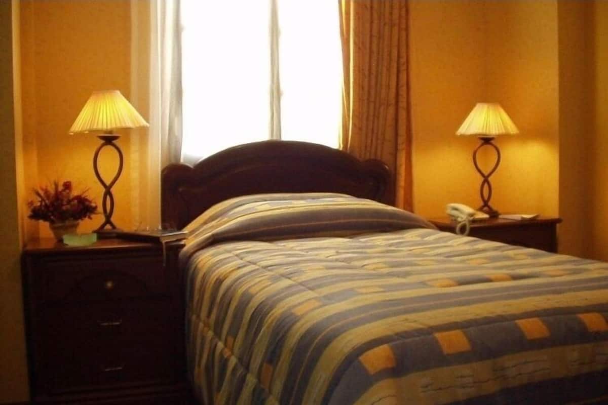 A hotel room with a bed, two bedside lamps, a nightstand, a telephone, and a window with curtains.