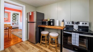 Une cuisine compacte équipée d’un réfrigérateur, d’un four à micro-ondes, d’une machine à café et d’une cuisinière. Elle comprend deux tabourets et un comptoir-bar en bois.