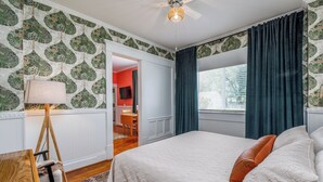 Une chambre à coucher avec un lit, un bureau, une lampe et une fenêtre avec des rideaux.