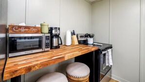 Une cuisine compacte équipée d’un four à micro-ondes, d’une machine à café et d’une enseigne en bois sur laquelle est écrit « Coffee Bar ».