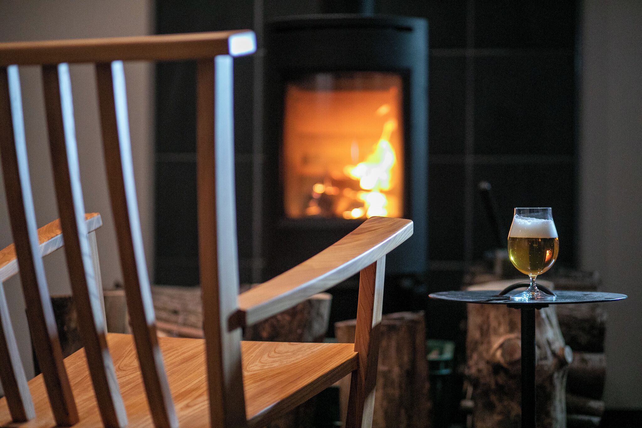 A wooden chair and a glass of beer in front of a fireplace.