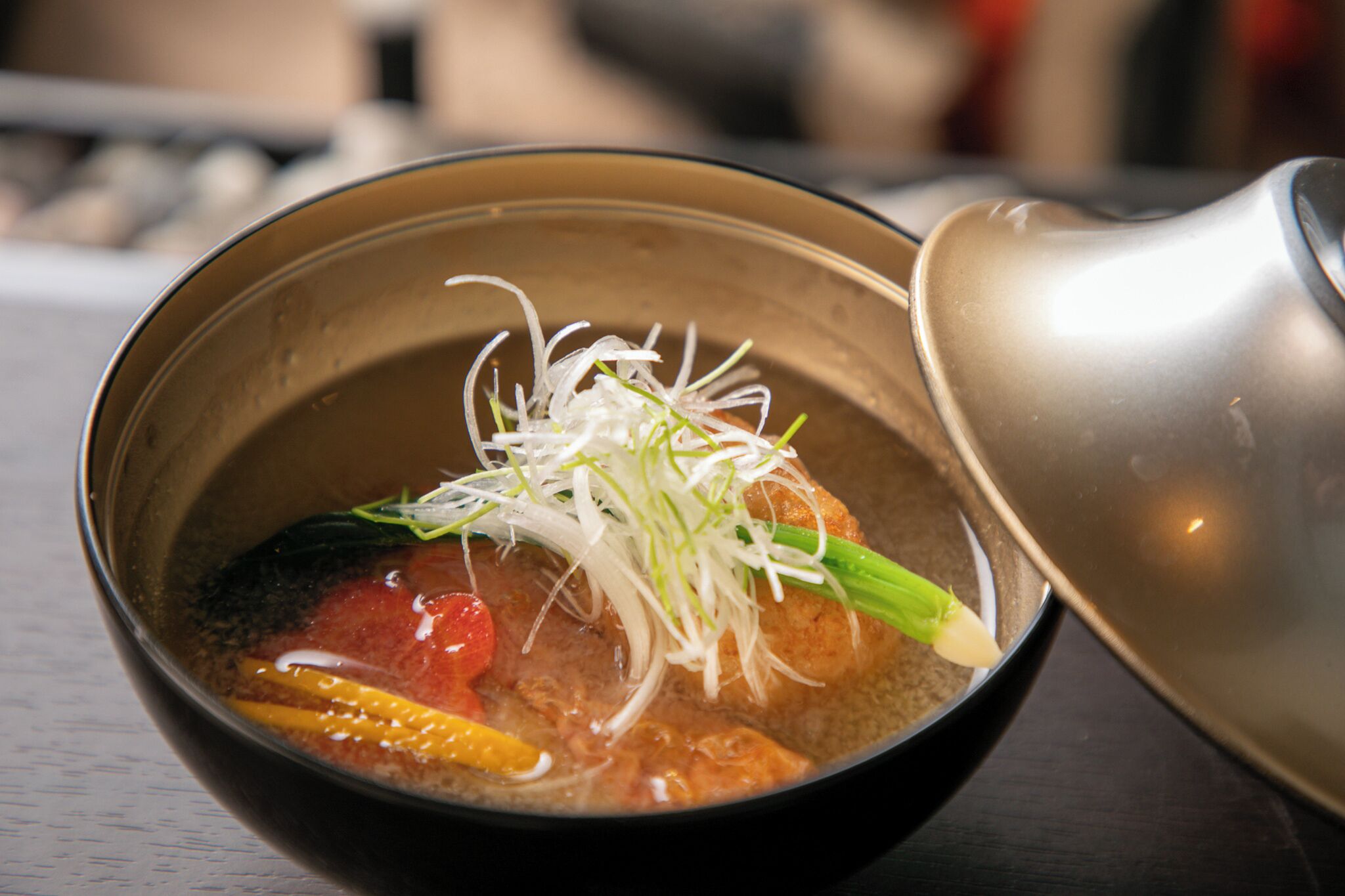 A bowl of soup with vegetables and a metal ladle.