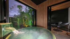 A modern spa room with a hot tub, wooden paneling, and a view of trees and mountains. - Bettei Fujiya (Hatsukaichi)