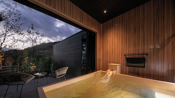 A modern indoor hot tub area with a wooden interior, a glass wall, and a view of the outdoors. - Bettei Fujiya (Hatsukaichi)