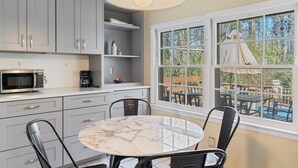 A kitchen with a round marble table and chairs, a microwave, and a coffee maker. - Designer Home - Pool - Billiards - Home Office (Cary)