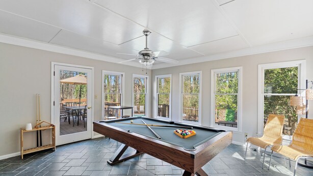 A pool table in a room with large windows, a ceiling fan, and a door leading to an outdoor area. - Designer Home - Pool - Billiards - Home Office (Cary)