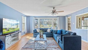 A modern living room with a large flat-screen TV, a ceiling fan, and a sofa set. - Designer Home - Pool - Billiards - Home Office (Cary)