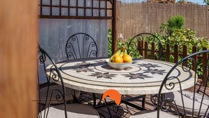 Een ronde tafel met een bloemmotief, een schaal vol fruit en metalen stoelen.