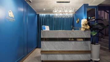 A hotel reception desk with a blue wall, a marble counter, a chandelier, and a sign indicating a room rate.