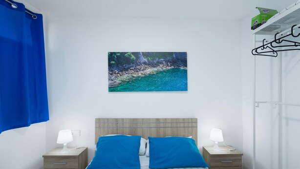 Ein Schlafzimmer mit einem Bett, zwei Nachttischen mit Lampen, einem Wandbild und einem Metallregal.
