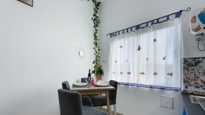 Ein Essbereich mit einem Tisch für vier Personen, Stühlen, einer Uhr an der Wand und einem Fenster mit Vorhang.