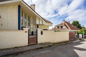 A residential house with a white exterior, a tiled roof, and a gated entrance.