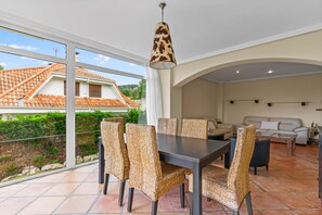 A dining area with a table and chairs, a hanging light fixture, and a view of a house with a tiled roof. - Holiday Home 'Villa De Lujo En Cantabria' with Mountain View, Wi-Fi and Air Conditioning (Cantabria)