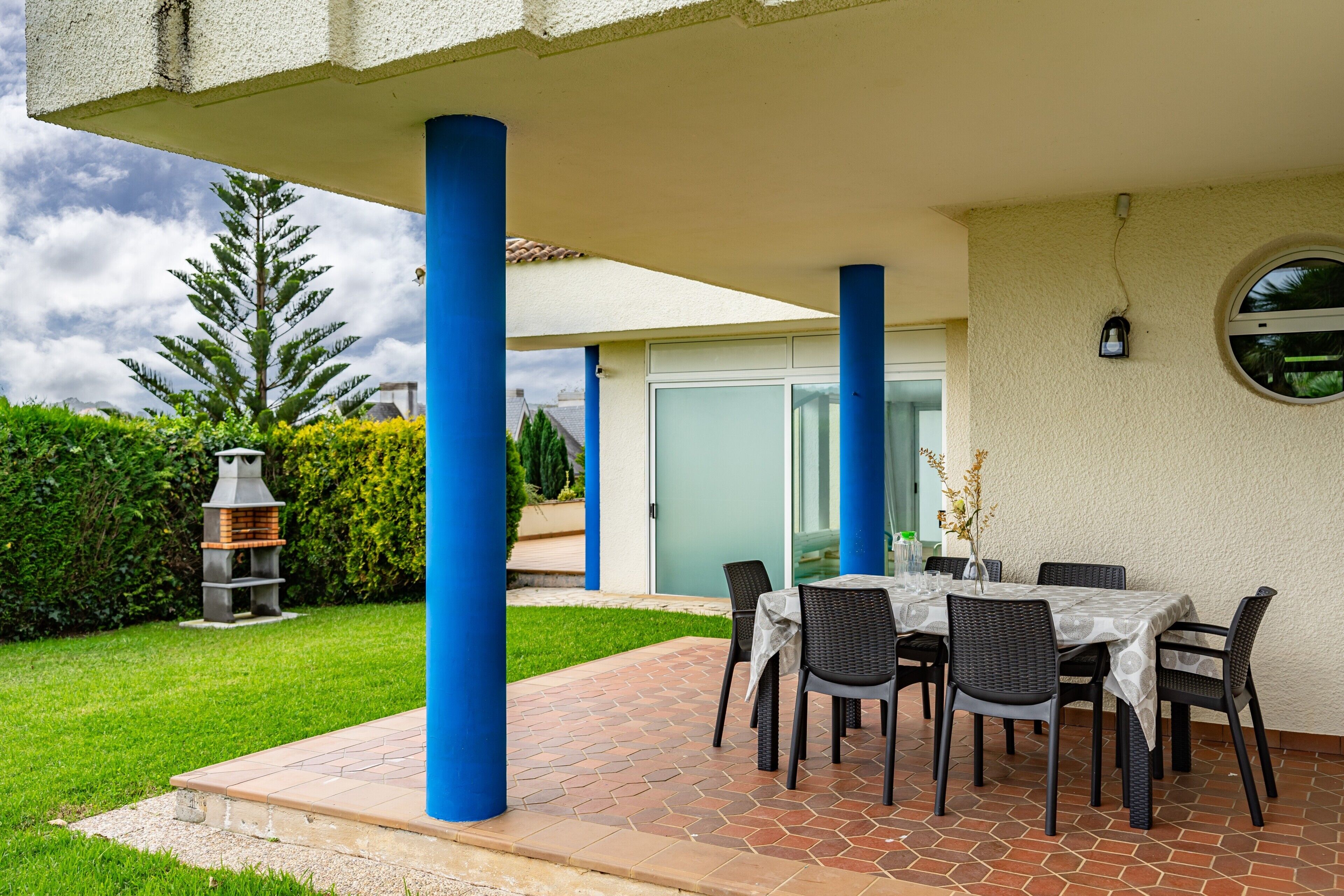 A patio with a table and chairs, a barbecue grill, and a covered area with blue columns.