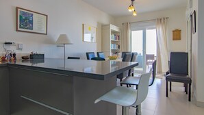 A modern kitchen with a central island, dining area with chairs, a bookshelf, and a view to a balcony. - Villa 'Casa Flores 047' with Sea Views, Wi-Fi and Air Conditioning (Almayate)