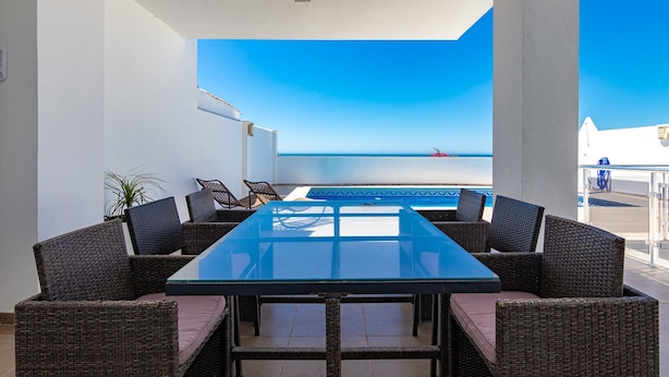 A covered outdoor seating area with a glass table and wicker chairs, overlooking a pool and a clear blue sky. - Villa 'Casa Flores 047' with Sea Views, Wi-Fi and Air Conditioning (Almayate)