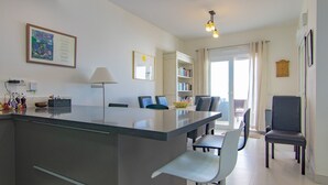 A modern kitchen with a central island, dining area with chairs, a bookshelf, and a door leading to a balcony. - Villa 'Casa Flores 047' with Sea Views, Wi-Fi and Air Conditioning (Almayate)