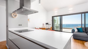 Een moderne keuken met een groot eiland, een ingebouwde kookplaat en uitzicht op de oceaan door grote ramen.