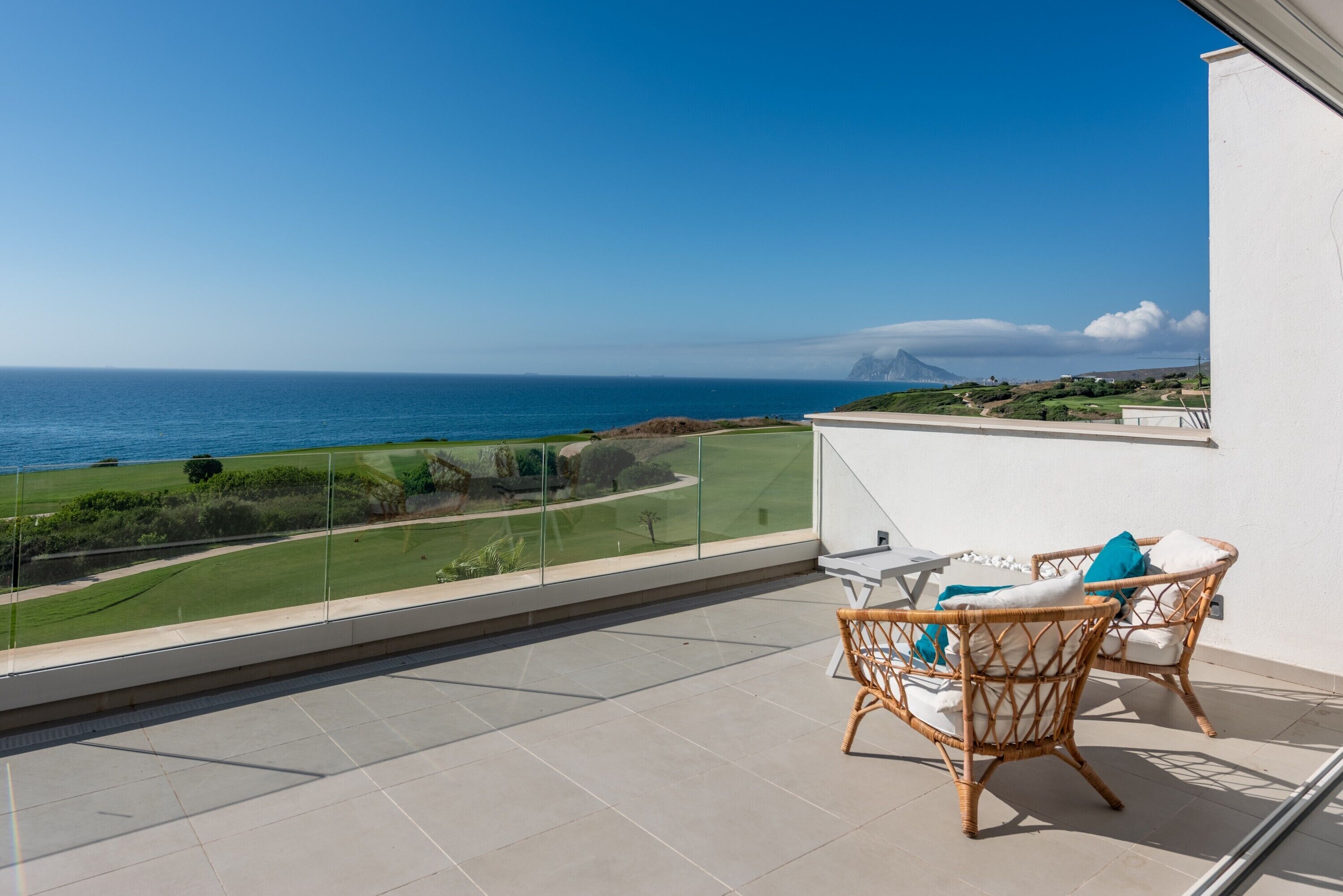 Ein Balkon mit Blick auf das Meer, Korbmöbel und eine weiße Wand.